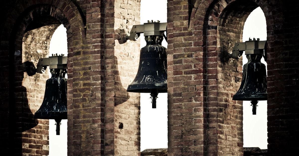 Historic bronze church bells hanging in the arched openings of a brick tower