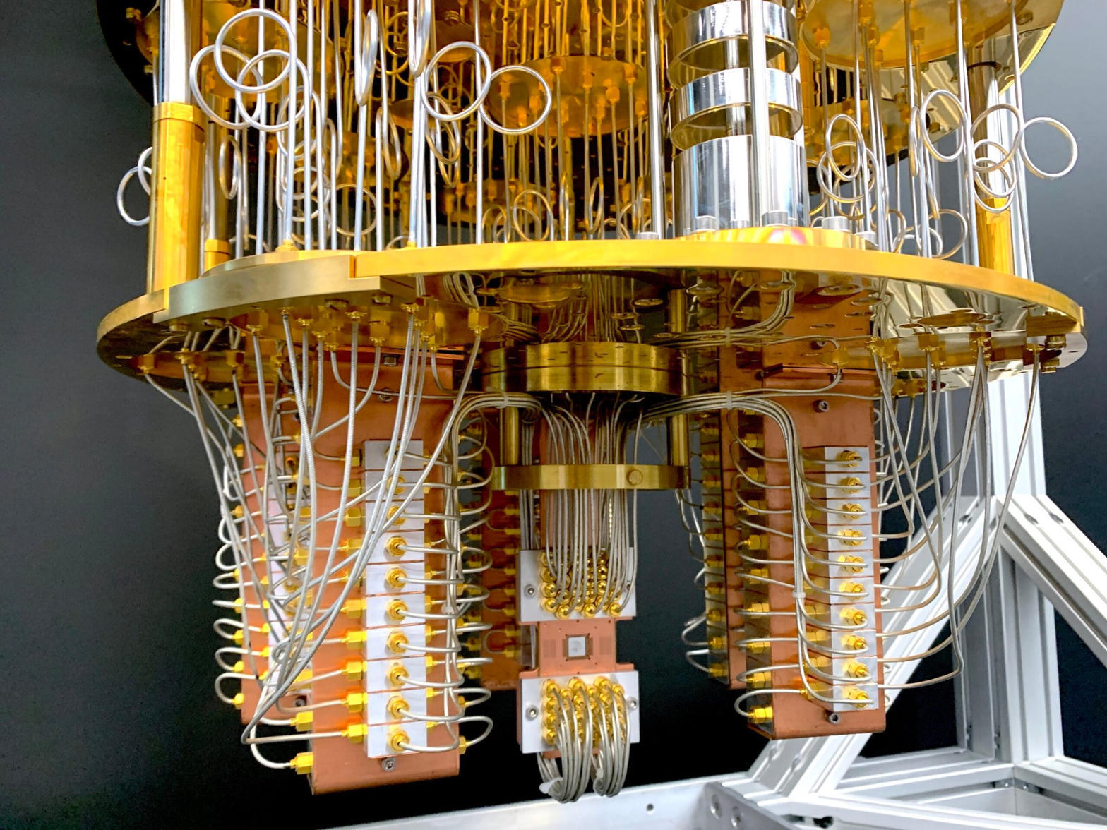 Gold and copper wiring stages of a superconducting quantum processor hanging inside a dilution refrigerator, with coaxial lines running down to the chip